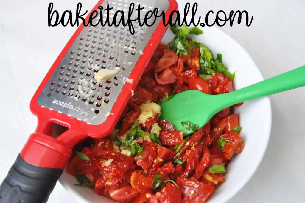garlic on a microplane grater over the bowl of tomato mixture