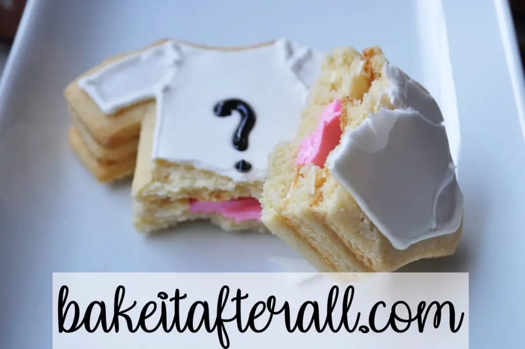stuffed sugar cookie with white onesie design on top with black question mark broken open to reveal pink filling inside