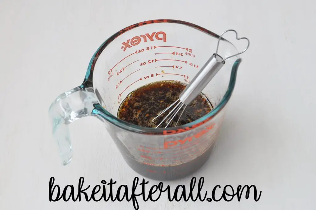 glass measuring cup filled with honey garlic marinade ingredients with a small wire whisk inside