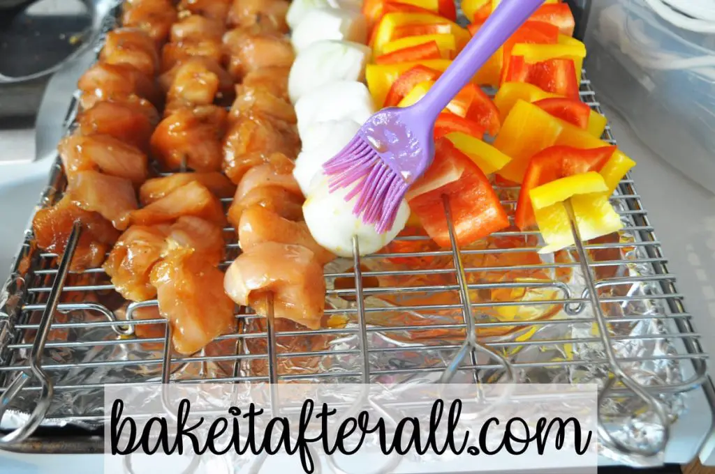 silicone pastry brush brushing marinade on onion skewer next to honey chicken kabobs