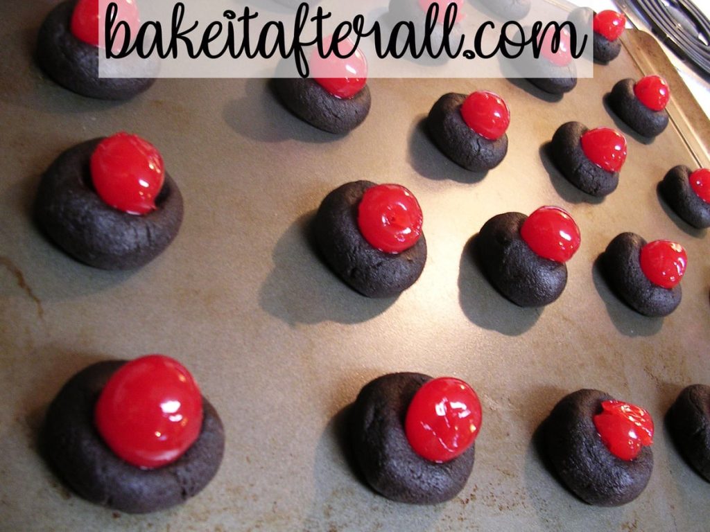 unbaked cookies with a maraschino cherry in the center of each cookie on a baking sheet