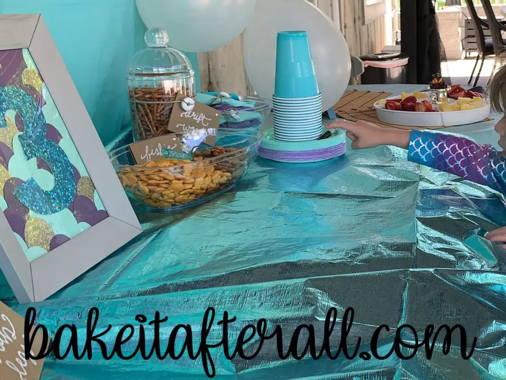 food table with a decorated mermaid picture frame and snacks