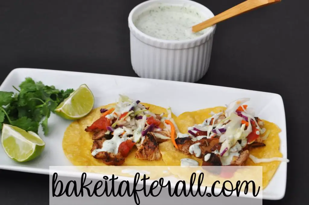 Cilantro Lime Crema Costco Copycat on top of Costco Chicken Street Tacos on a plate with limes and cilantro garnish
