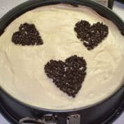 a red velvet cheesecake in a springform pan with cream cheese frosting on top and chocolate chips in the shape of hearts