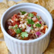 Rotel tomatoes and corn salsa in a white ramekin surrounded by tortilla chips