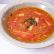 a bowl of chicken, leek and tomato soup with fresh basil on top