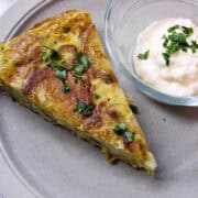 a wedge of tortilla espanola on a plate with a small dish of garlic mayonnaise