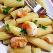 a white plate with garlicky shrimp pasta on top and a metal fork on the side