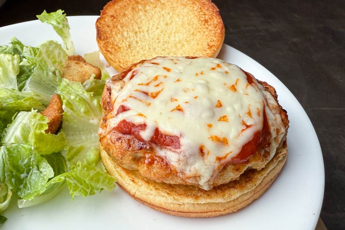 Chicken Parmesan Burgers on a white plate with salad