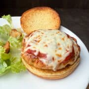 Chicken Parmesan Burgers on a white plate with salad