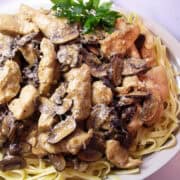 a platter of Chicken with Dijon Mascarpone Marsala Sauce on top of a bed of fettucine with a small bunch of parsley leaves