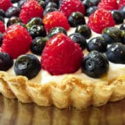 a fresh berry tart on a silver platter with fresh blueberries and raspberries on top