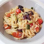 a bowl of orzo with tomatoes, zucchini and olives