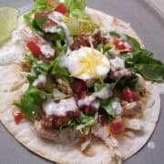chicken tostada on a plate with cilantro lime drizzle on top