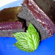 dark chocolate mascarpone brownies with blueberry ganache stacked on top of each other on a blue plate with 3 mint leaves in front