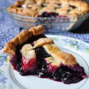 a slice of Fresh Blueberry Pie on a china plate with the pie plate in the background