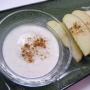 honey yogurt dip in a bowl next to slices of apples sprinkled with cinnamon