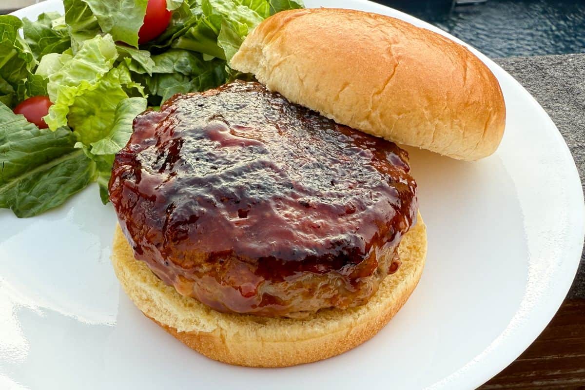a pepper jack stuffed turkey burger on a bun on a white plate with salad behind it