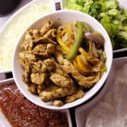 honey lime chicken fajitas in a white bowl surrounded by fajita toppings