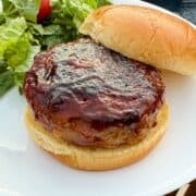 a pepper jack stuffed turkey burger on a bun on a white plate with salad behind it