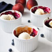 Peach blueberry crumbles with ice cream on top in white ramekins