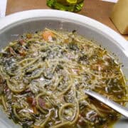 ribollita soup in bowl with a spoon on a cutting board with cheese and cracker