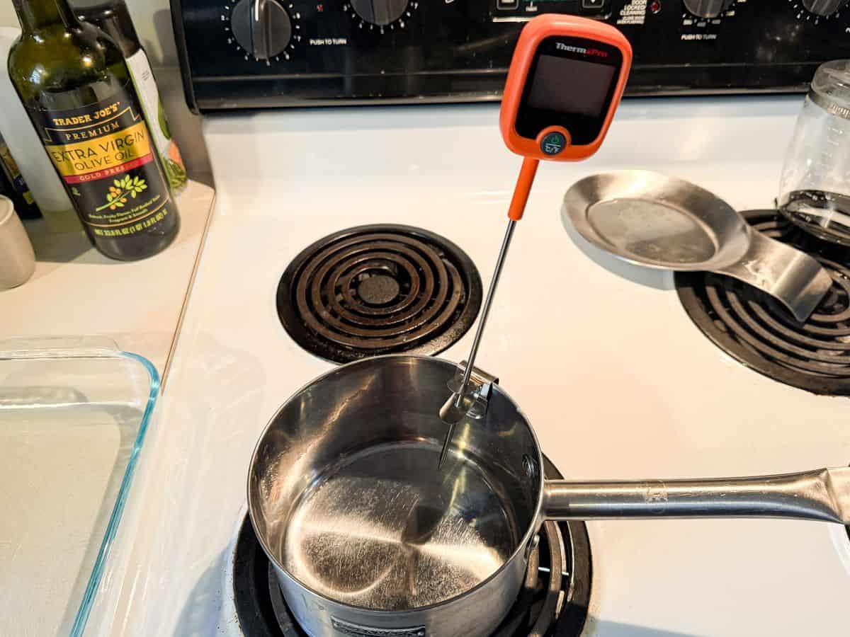 a saucepan on a stove with a digital candy thermometer clipped to the side