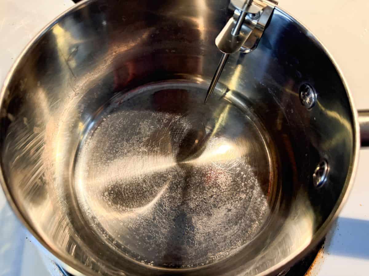 a saucepan on a stove with a digital candy thermometer clipped to the side