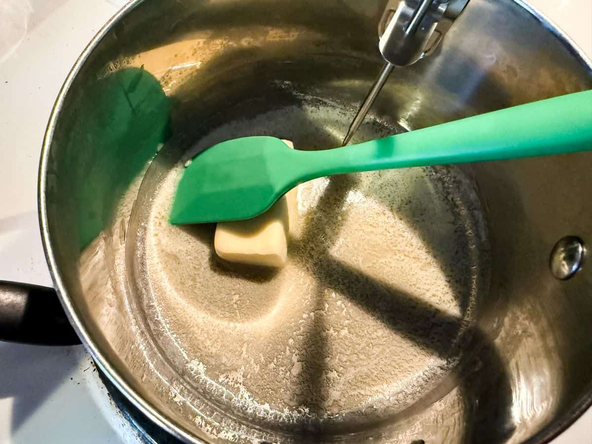 a small saucepan with butter melting and being stirred with a small green silicone spatula