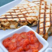 chicken and spinach quesadillas with grill marks on a white plate and a dish of salsa