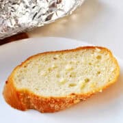 garlic bread on a white plate with the rest of the loaf in aluminum foil behind it