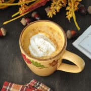 a pumpkin latte on a wood surface with a book and fall foliage around it