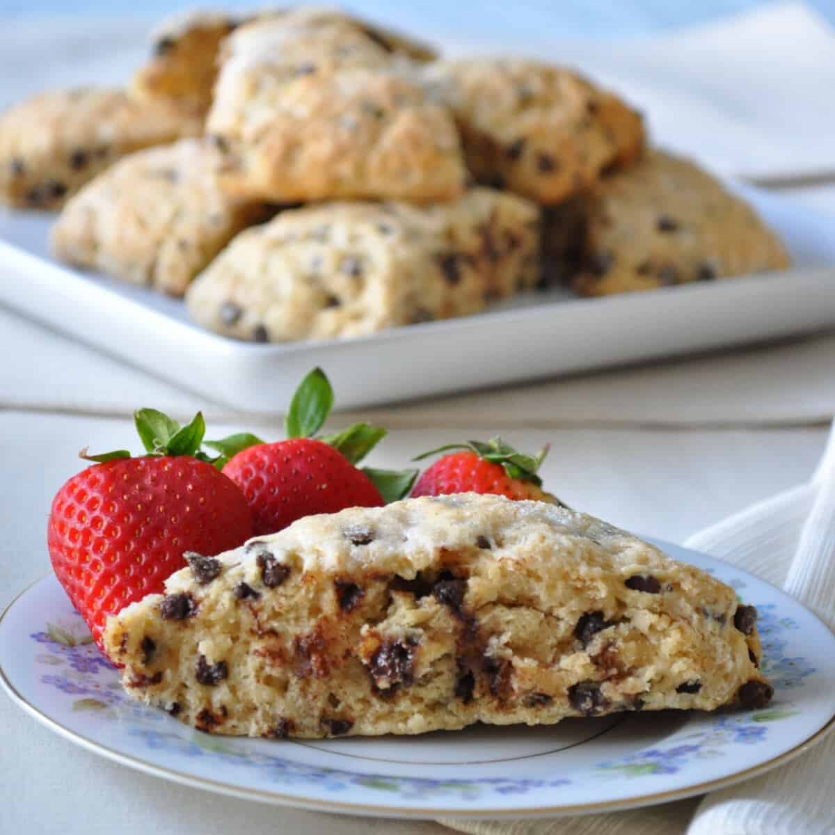 Skinny Chocolate Chip Scones on a platter in the background with one on a plate with strawberries in the foreground