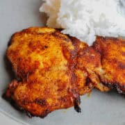 spicy honey brushed chicken thighs on a plate with rice behind them