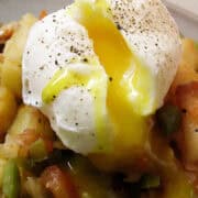 a poached egg cut open over crispy potatoes skillet with the yolk running down