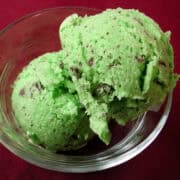 a clear bowl with two scoops of mint chocolate chunk ice cream on a red background