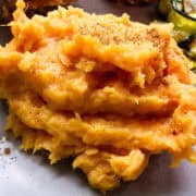 smashed sweet potatoes on a plate with zucchini in the back