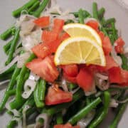 Haricots Verts with Shallots on a plate with tomatoes and lemon slices on top