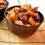 Bourbon chicken over rice in brown bowls with metal chopsticks on top of wooden placemats