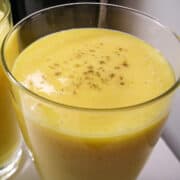 a homemade mango lassi in a glass with spice sprinkled on top