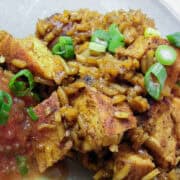 Red chili chicken and rice on a plate with sliced green onions on top