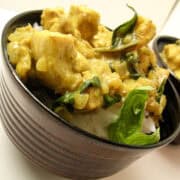 a bowl of coconut curry chicken garnished with fresh basil