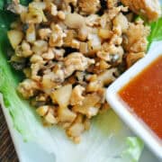 chicken lettuce wrap on a white plate with a white dish of dipping sauce