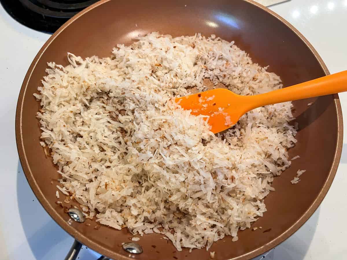 sweetened coconut in a saute pan with a small silicone spatula half way through toasting