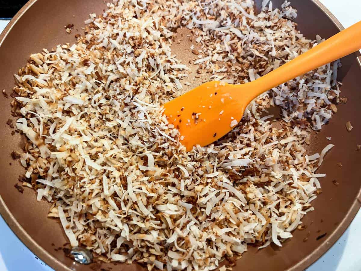 toasted sweetened coconut in a saute pan with a small silicone spatula