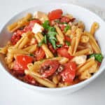 a bowl of pasta with sun dried tomatoes, mozzarella cheese and basil