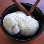 scoops of homemade cinnamon ice cream in a bowl with cinnamon sticks on a wood table