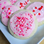 soft frosted sugar cookies with pink frosting and Valentine sprinkles on a white plate