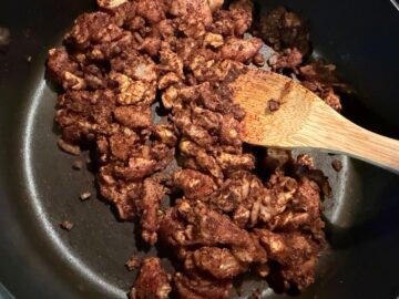 diced chicken breast sauteing in pan with enchilada seasoning and a wooden spoon stirring