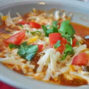 a bowl of simplified chicken tortilla soup topped with shredded cheese, chopped tomatoes, and chopped cilantro